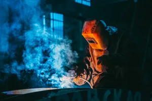 Artisan soudeur au masque de protection, fumée bleutée